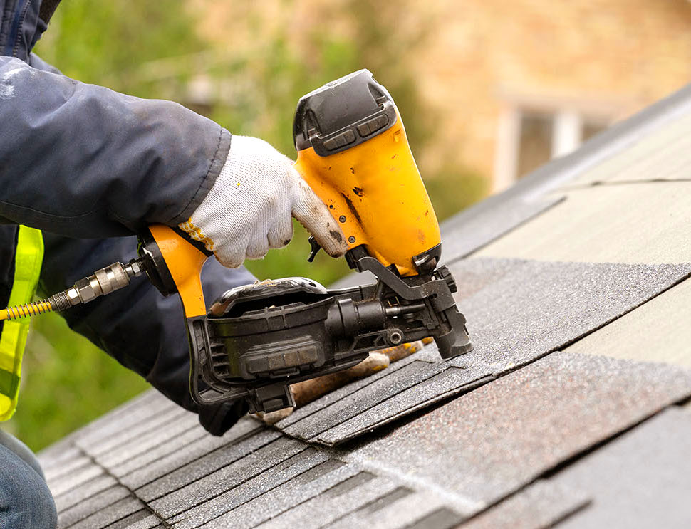 An image of a roofer nailing shingles on the roof.